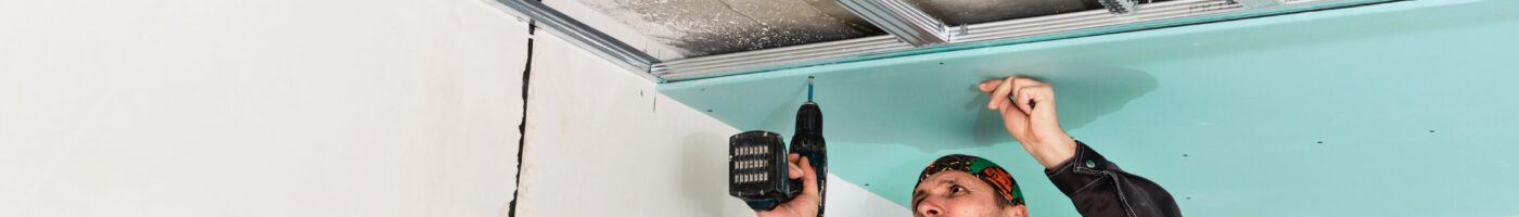 Construction worker assembly suspended ceiling with drywall and fixing the drywall to the ceiling metal frame with screwdriver.